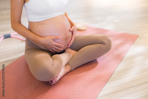 Pregnant woman sitting on yoga mat indoors