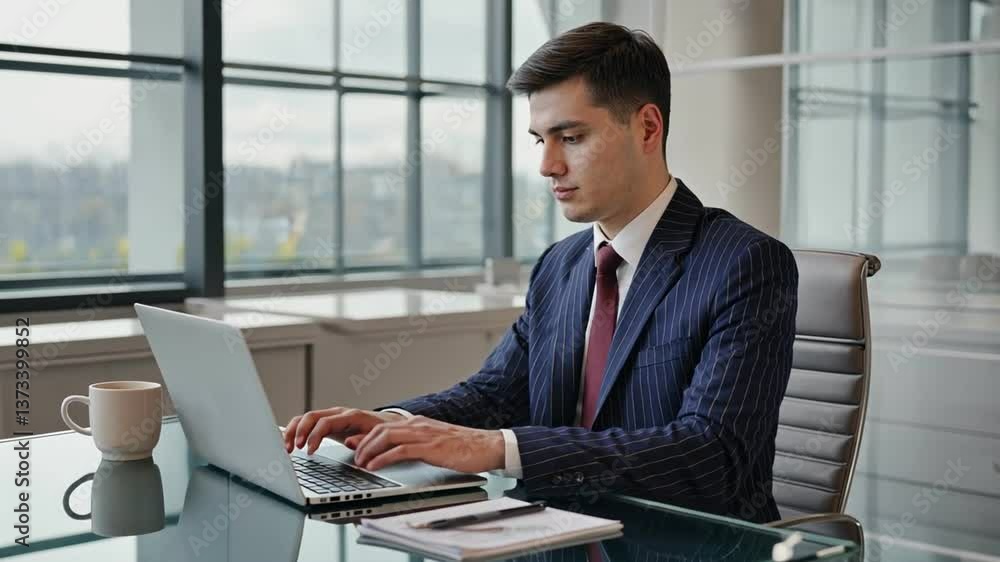 Modern Professional at Work: A focused businessman, suited in a business-ready ensemble, navigates his laptop in an modern office environment. Modern Professional at Work: A focused businessman, suited in a business-ready ensemble, navigates his laptop in an modern office environment.