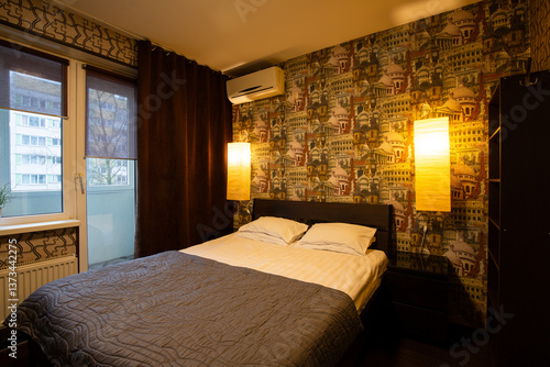 Obraz na płótnie Apartment interior. Bedroom. Pillows and bedspread on the made bed. Wallpaper with images of European landmarks. Air conditioning and wall lamps on the wall. Window in the wall and door to the balcony w salonie