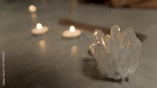 Close-up of a white transparent crystal standing near burning candles in the background. The beautiful stone shimmers in the light.