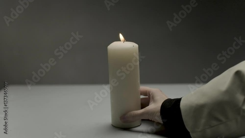 The girl carefully moves a large long candle with a small bright yellow flame deep into the table. Peace and tranquility from a burning light
