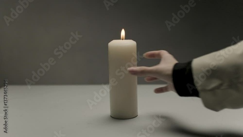 The girl carefully turns a large long candle with a small bright yellow flame deep into the table in a circle. Peace and tranquility from a burning light