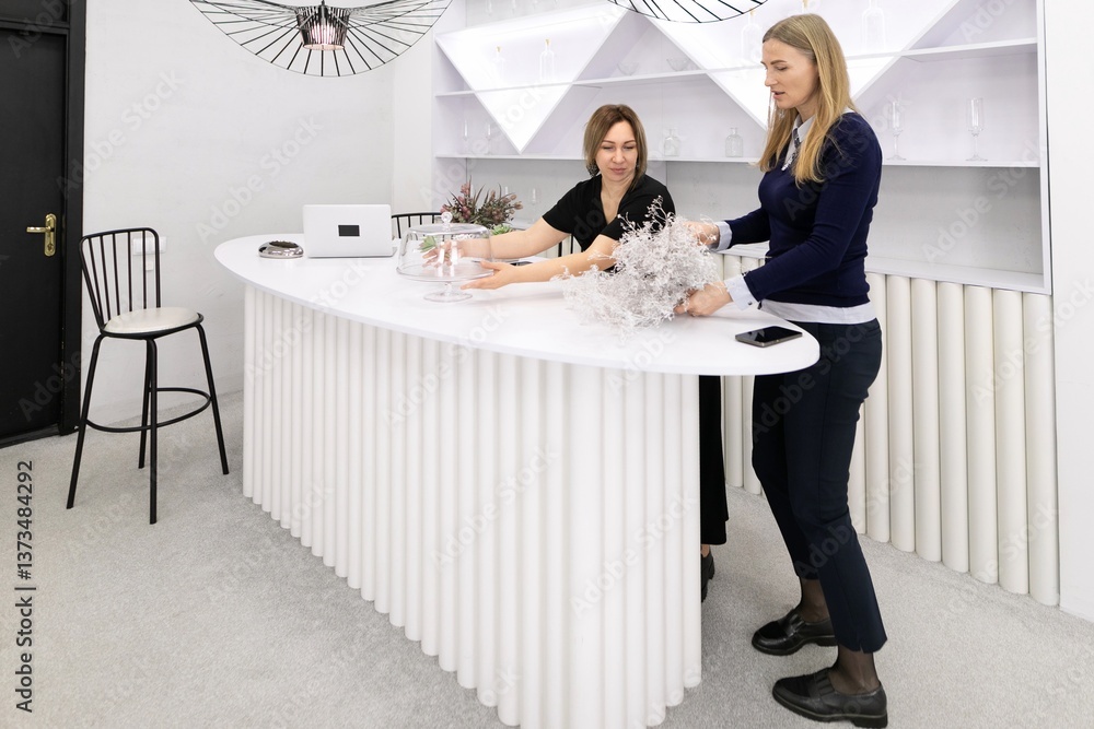 Two women engage in creative decoration at a modern counter in a stylish interior space designed for floral arrangements and events