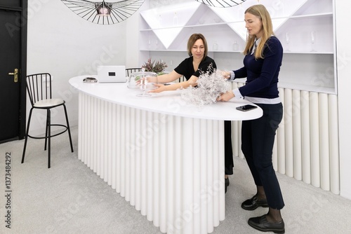 Obraz na płótnie Two women engage in creative decoration at a modern counter in a stylish interior space designed for floral arrangements and events w salonie