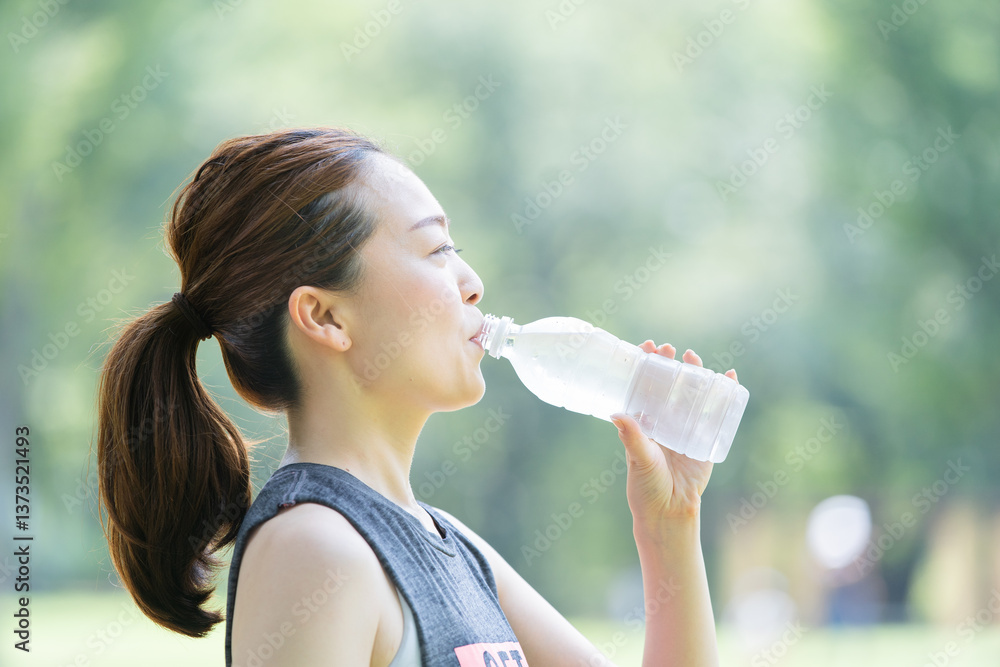 公園で運動(ヨガ)中に水分を補給する女性 公園で運動(ヨガ)中に水分を補給する女性