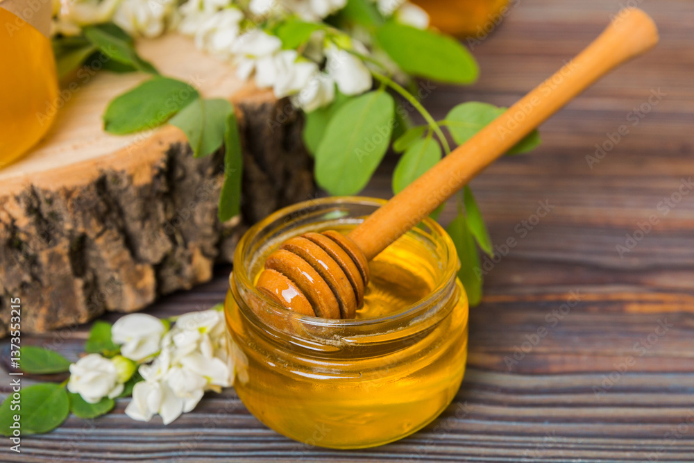 Fototapeta premium Sweet honey jar surrounded spring acacia blossoms. Honey flows from a spoon in a jar. jars of clear fresh acacia honey on wooden background