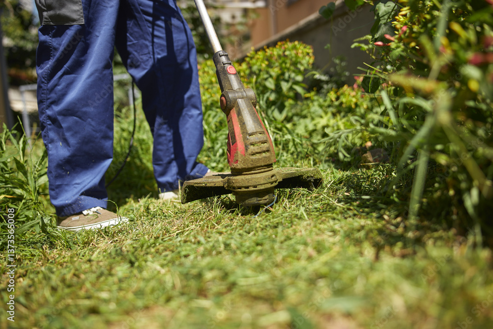 Gardener with a grass trimmer cutting overgrown grass and weeds