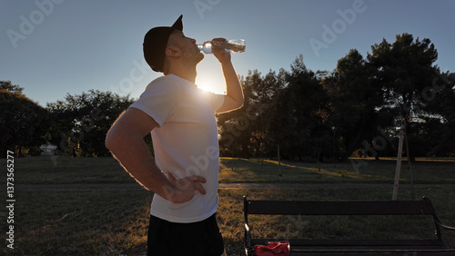 Obraz na płótnie Thirsty man drinking water after jogging in a park during sunset hours. w salonie