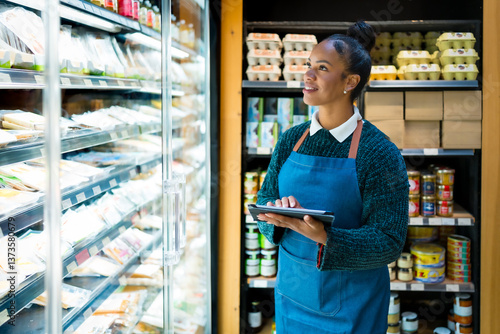 Cuadro en lienzo Saleswoman using digital tablet checking food products in refrigerator at organi