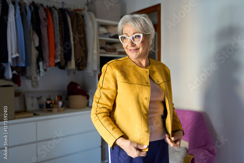 Obraz na plátne Senior woman wearing yellow jacket choosing clothes from closet at home