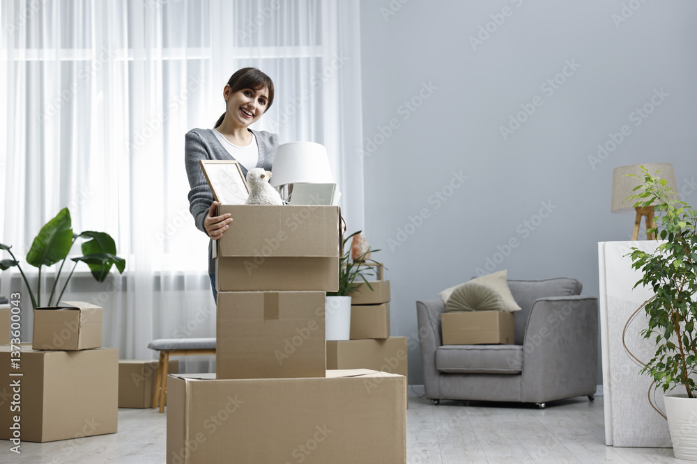Fototapeta premium Moving day. Happy woman with her belongings in new home, space for text