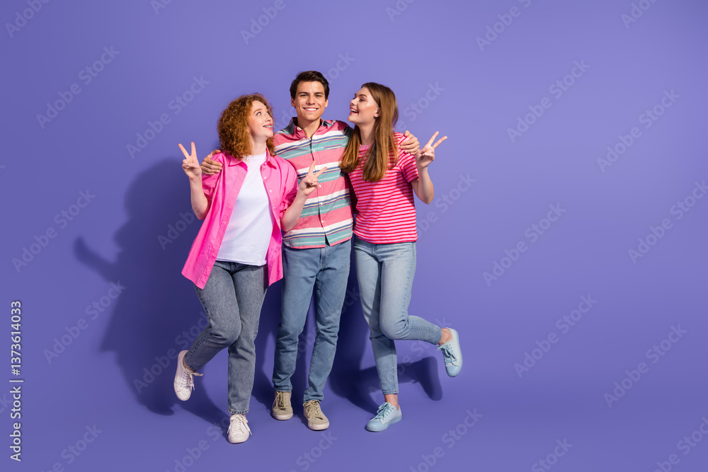 Fototapeta premium Three cheerful young friends posing joyfully against a purple background showcasing casual style and friendly gestures.