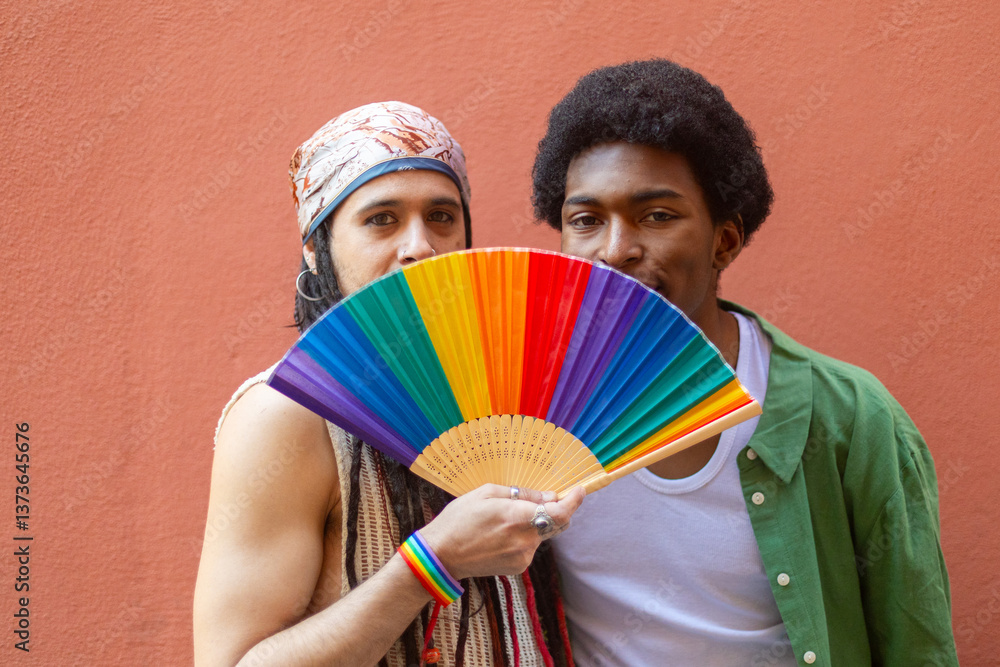 Obraz premium Gay couple hiding behind rainbow fan celebrating pride month