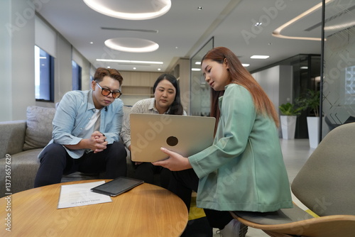Obraz na płótnie A 29-year-old Asian woman in a suit holds a laptop explaining the terms and conditions of life insurance to male and female customers in an office lounge. w salonie