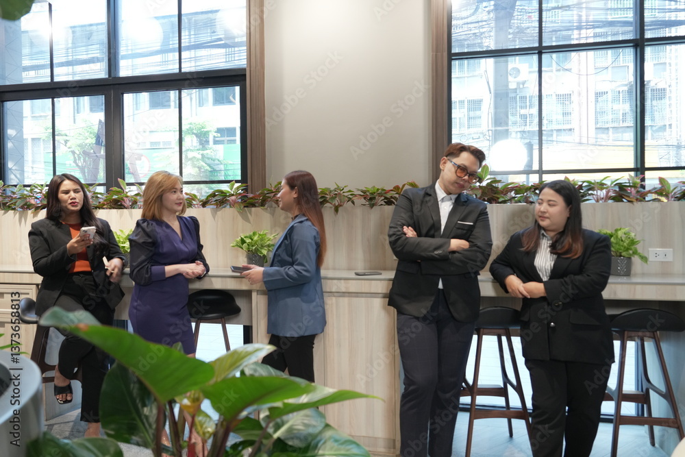 A team of Asian male and female employees in business suits take a break and chat with each other in the company lobby.
