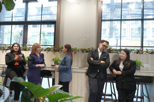 A team of Asian male and female employees in business suits take a break and chat with each other in the company lobby.