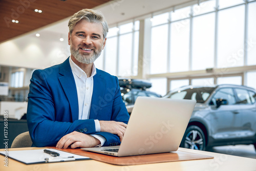 Businessman in suit sitting in automobile dealership office using laptop