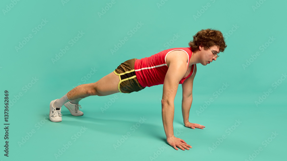 Man holding full plank position on floor, maintaining strong posture and straight back against mint studio background. Concept of full-body exercise, core stability, strength workout, physical fitness Man holding full plank position on floor, maintaining strong posture and straight back against mint studio background. Concept of full-body exercise, core stability, strength workout, physical fitness