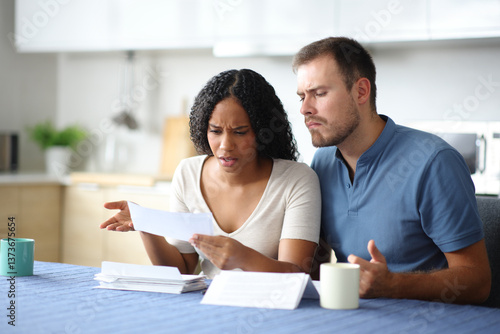 Photography Angry interracial couple reading bank statement in the kitchen