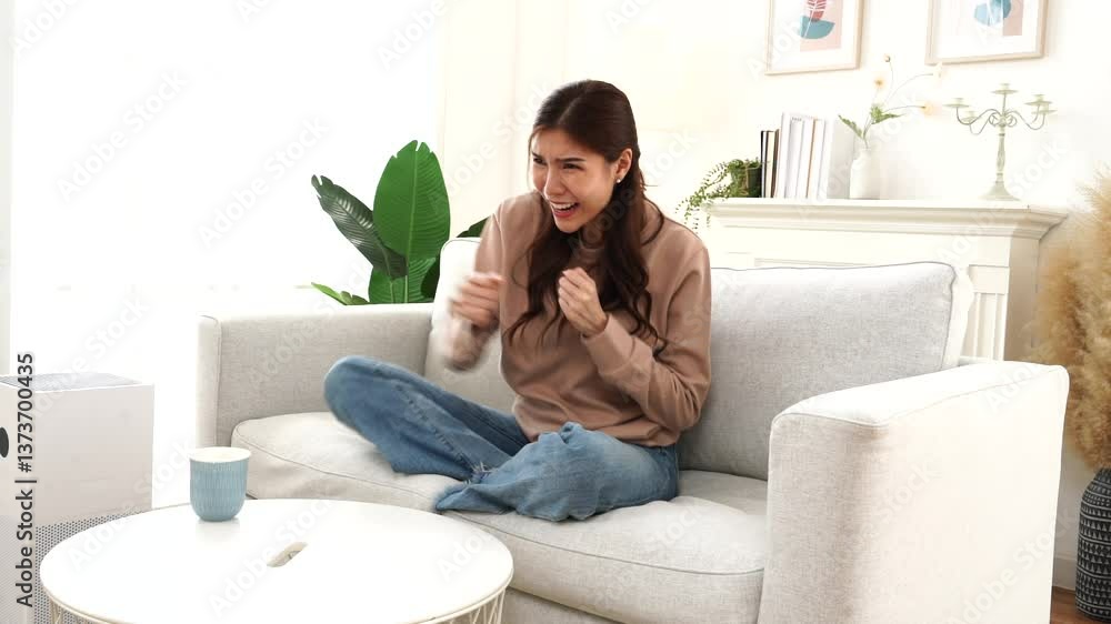 Asian woman sitting on sofa cheering on sports watching TV on holiday in living room at home Asian woman sitting on sofa cheering on sports watching TV on holiday in living room at home