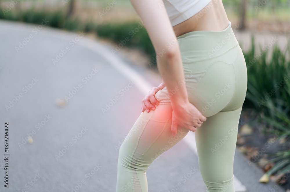 custom made wallpaper toronto digitalyoung Asian woman experiencing pain her thigh during exercise outdoors, holding her leg with discomfort. She is wearing light green leggings and white top, standing paved path surrounded by