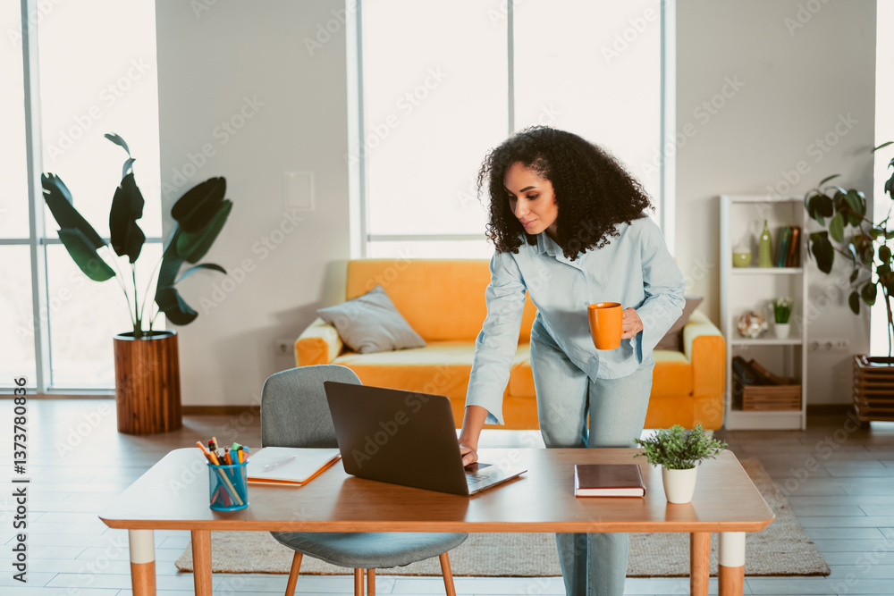 Young woman in casual attire working on a laptop at home, enjoying coffee and a vibrant, comfortable interior in an apartment Young woman in casual attire working on a laptop at home, enjoying coffee and a vibrant, comfortable interior in an apartment