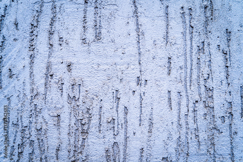 Close-up photo of a rough stucco wall painted in light blue, featuring vertical streaks and uneven surface texture. The wall has a tactile, gritty appearance with weathered imperfections 