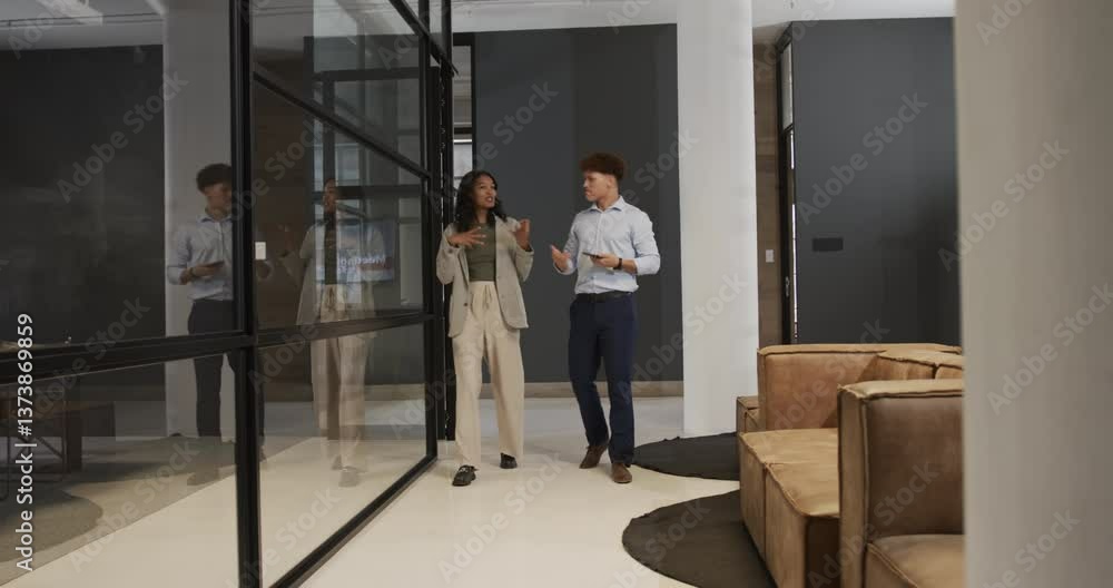 Discussing work, business diverse professionals walking in modern office holding documents Discussing work, business diverse professionals walking in modern office holding documents