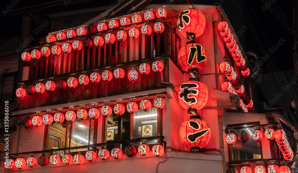 Fototapeta premium Illuminated Osaka Japanese Yakiniku restaurant at night. Numerous red paper lanterns with Japanese characters adorn the building.