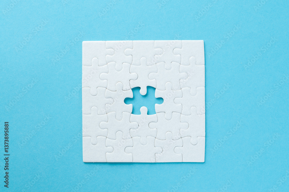 Concept for problem-solving, teamwork, solutions, or missing connections. White jigsaw puzzle on a vibrant blue background with one missing piece. Minimalist composition with copy space. Concept for problem-solving, teamwork, solutions, or missing connections. White jigsaw puzzle on a vibrant blue background with one missing piece. Minimalist composition with copy space.