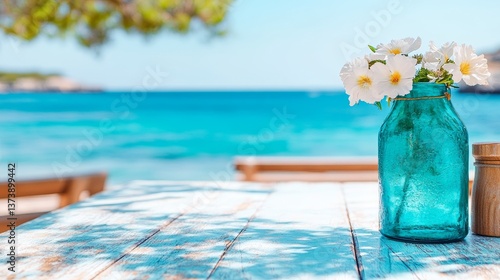 turquoise glass vase with white flowers casting shadows on wooden table near ocean under clear summer sky