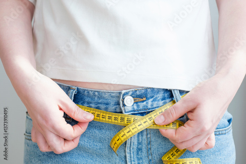 Obraz na płótnie Measuring tape as belt in jeans close-up on a gray background.