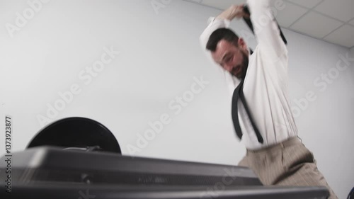 A businessman in aggression loses his temper in a fit of rage. An enraged office worker smashes a computer monitor with his keyboard, throws things off his desk and screams. Financial crisis or layoff