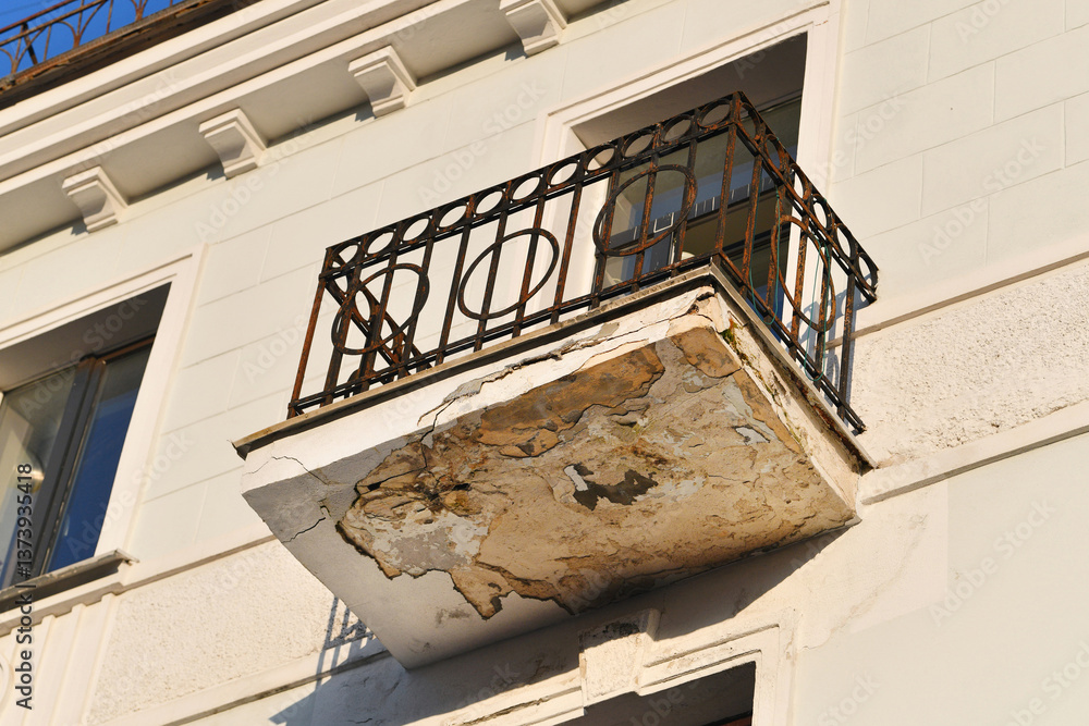 Historic building with damaged balcony, rusted ironwork and peeling concrete, infrastructure deterioration. Decayed residential balcony with structural damage and corroded metal railing. Wear and tear