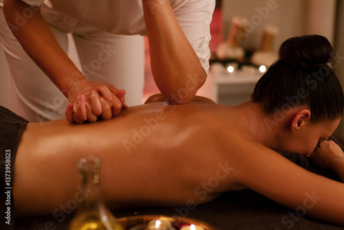 Professional massagist at health center using elbow for therapeutic remedial shiatsu technique spine back massage to help young woman