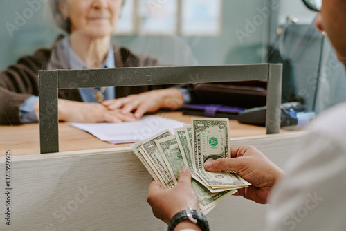 Obraz na płótnie Senior bank clerk handling financial transaction for customer across glass divid
