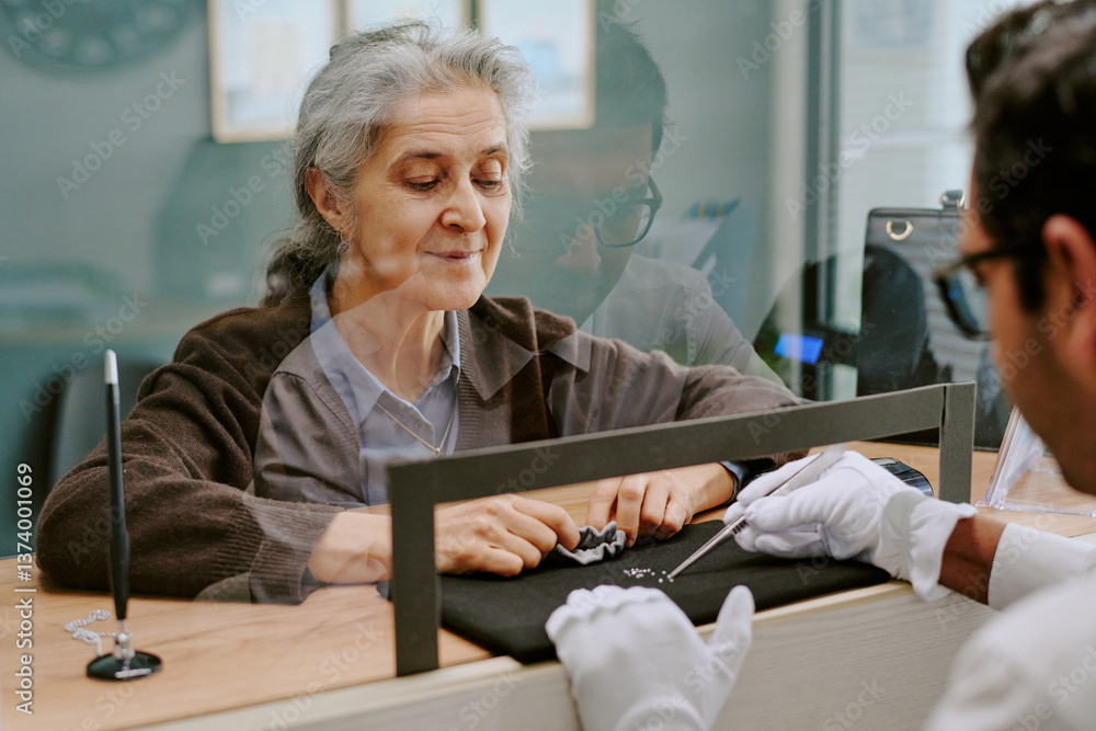 Obraz premium Elderly woman carefully examining pieces of jewelry at counter with jeweler's assistance, reflecting thoughtful consideration