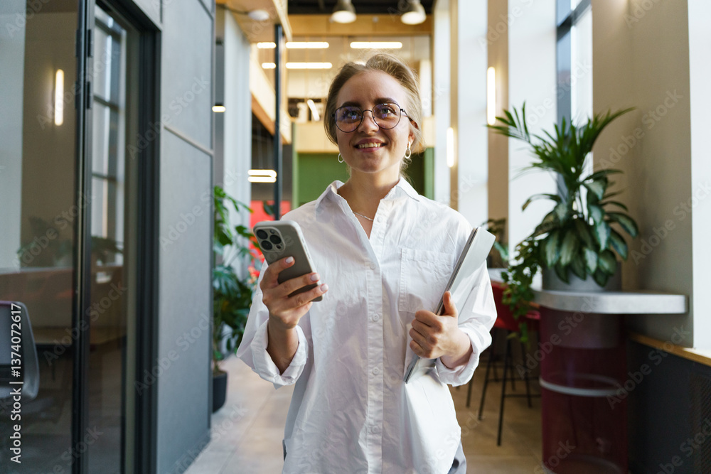 Young professional woman smiling while using smartphone in modern office interior during daytime Young professional woman smiling while using smartphone in modern office interior during daytime