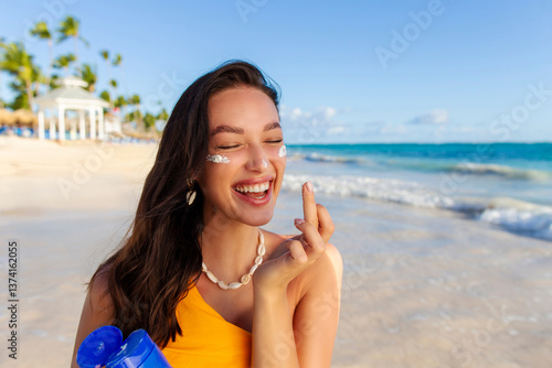 Fotografía Cheerful tanned lady putting sunscreen on her face, wearing swimsuit, standing on sandy beach on tropical ocean shore resort