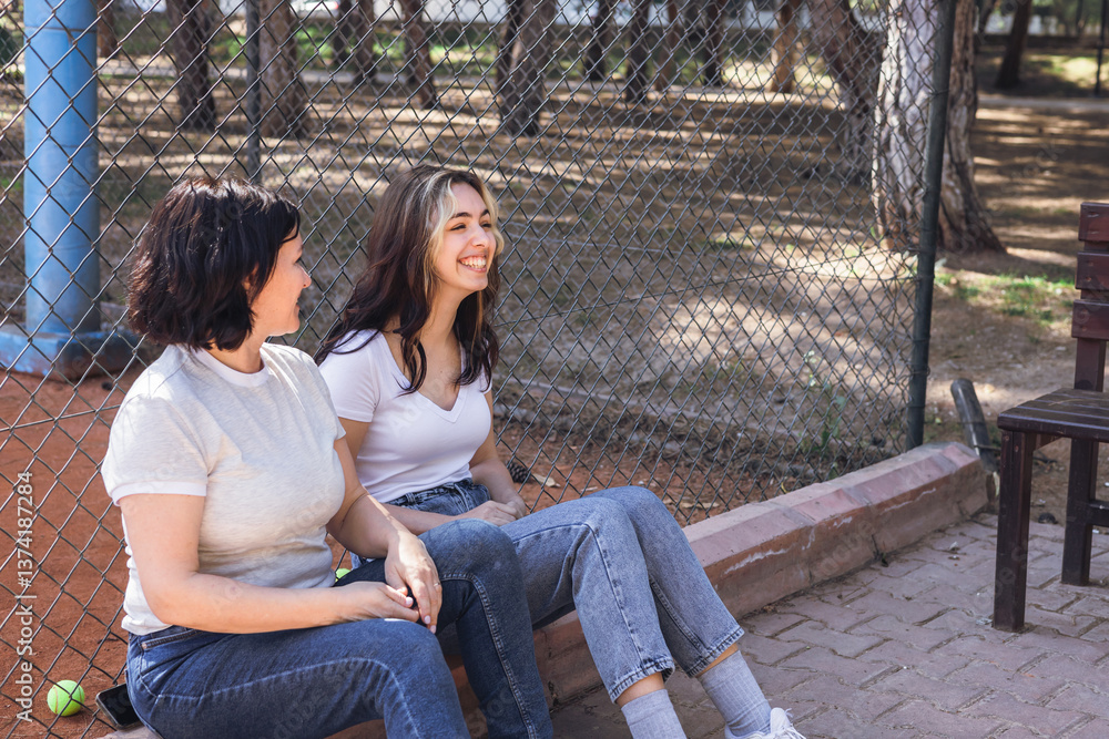 Women enjoying a conversation while resting near a tennis court during a sunny day Women enjoying a conversation while resting near a tennis court during a sunny day