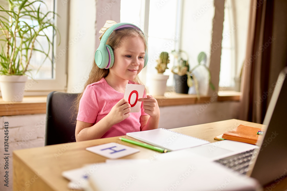 Curious girl leaning on desk and watching laptop screen with teacher leading lesson attentively during online class. Child studying at home in well lit room. Concept of education, childhood Curious girl leaning on desk and watching laptop screen with teacher leading lesson attentively during online class. Child studying at home in well lit room. Concept of education, childhood