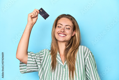 Young blonde woman holding a credit card in a studio