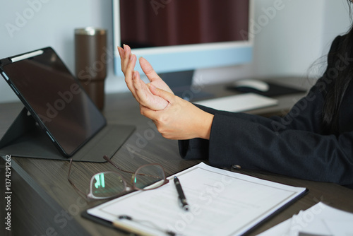 Fényképezés An asian tired business woman working for a long time and typing the computer, and using the mobile phone, so her wrist is hurt and she is massaging her hurt wrist by another hand, an office syndrome