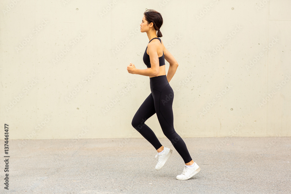 Fototapeta premium full length profile of sporty Asian woman running outdoors by urban wall