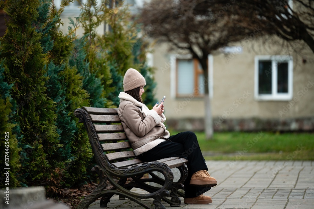 Fototapeta premium Person enjoying a quiet moment on a park bench while engaging with a mobile device amidst lush greenery and cozy surroundings