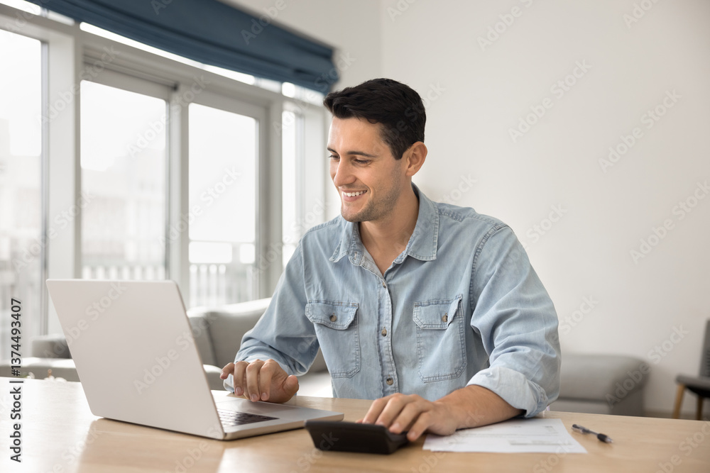 Young man sits at desk, smiling, working on budget, or calculating summary to pay related to his work or personal tasks, busy in household family financial management, take care of finances or savings Young man sits at desk, smiling, working on budget, or calculating summary to pay related to his work or personal tasks, busy in household family financial management, take care of finances or savings