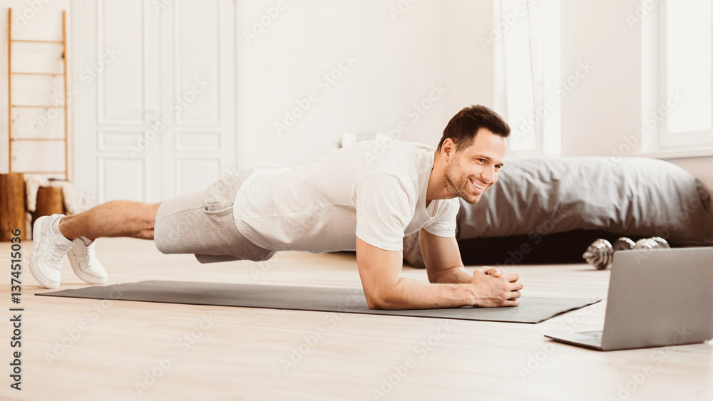 Home Training. Man Exercising At Laptop Doing Plank During Online Workout Indoors. Panorama Home Training. Man Exercising At Laptop Doing Plank During Online Workout Indoors. Panorama