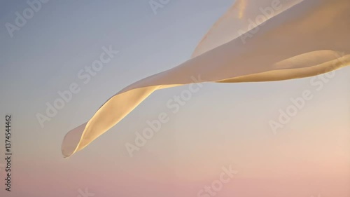 feather on the sky background, A light, white fabric dances in the soft winds against a peaceful sunset backdrop, creating a beautiful contrast with the soft colors of the sky. The fabric moves 