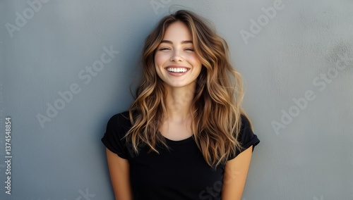 Smiling Woman Stands Confidently Against a Gray Wall in Casual Attire During ...