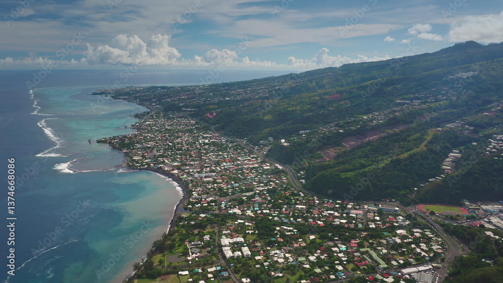 Fototapeta premium Breathtaking aerial view showcasing the stunning coastline of Tahiti, with colorful houses nestled between the vibrant turquoise ocean and the lush green slopes of the mountains, under a cloudy sky